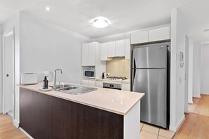 A modern kitchen with a central island, stainless steel appliances, and white cabinetry. - Inner City Action! 3bed/2bath/1car/3balconies (Brisbane)