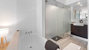 Uma casa de banho moderna com chuveiro em cabine de vidro, banheira e toucador com espelho.