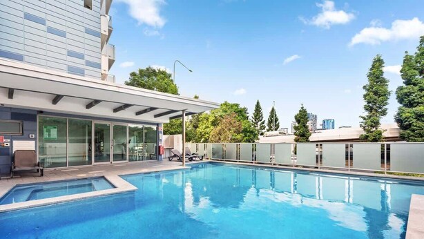 Um edifício moderno com piscina, portas de vidro e área de estar coberta.