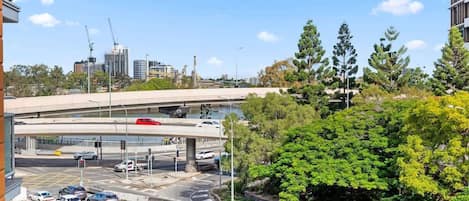 A multi-level parking structure with vehicles, a bridge, and urban buildings in the background.