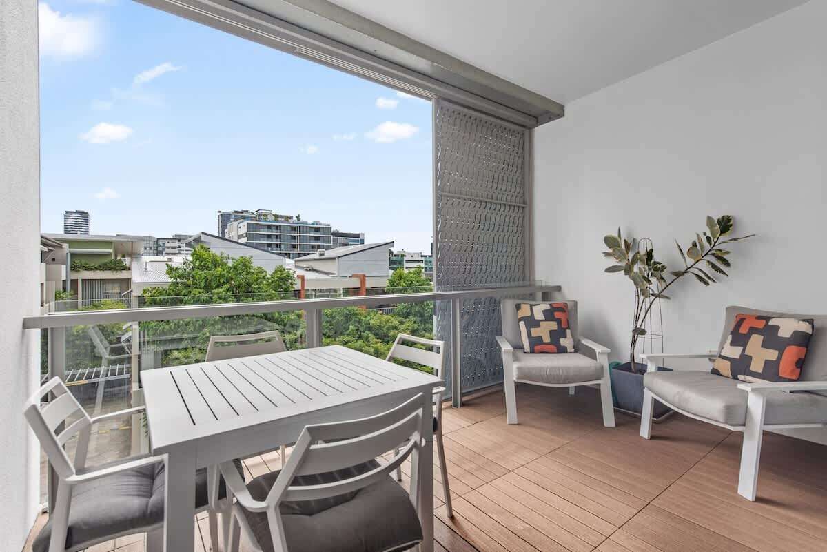 A balcony with a table and chairs, a potted plant, and a view of buildings.