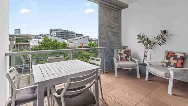 A balcony with a table and chairs, a potted plant, and a view of buildings. - Central & Stylish! 1bed/1bath/1car ~ 5 Mins to CBD (Brisbane)