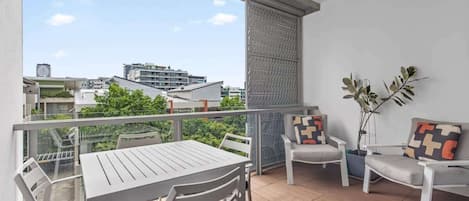 A balcony with a table and chairs, a potted plant, and a view of buildings.