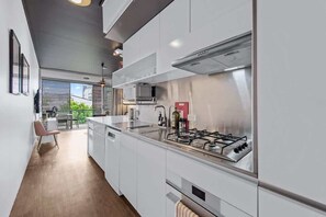 A modern kitchen with white cabinetry, a gas stove, and a view to an outdoor area. - Central & Stylish! 1bed/1bath/1car ~ 5 Mins to CBD (Brisbane)