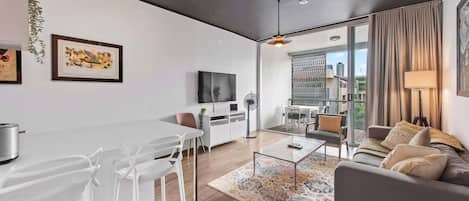 A modern living room with a dining area, a sofa, a TV, and artwork on the walls.