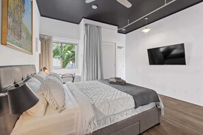 Une chambre moderne avec un lit, une télévision, un ventilateur de plafond et une fenêtre avec des rideaux.