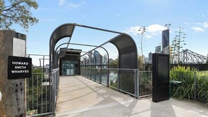 A pedestrian bridge with a metal arch structure, a sign reading 'HOWARD SMITH WHARVES,' and a cityscape in the background. - City Living! 1bed/1bath/pool (Brisbane)