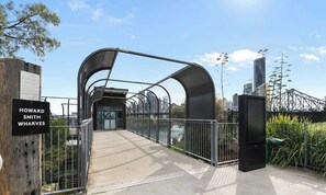 A pedestrian bridge with a metal arch structure, a sign reading 'HOWARD SMITH WHARVES,' and a cityscape in the background. - City Living! 1bed/1bath/pool (Brisbane)