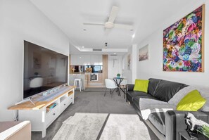 A modern living room with a flat-screen TV, a black leather sofa, a dining table, and a kitchen in the background. - City Living! 1bed/1bath/pool (Brisbane)