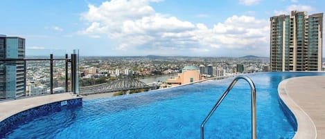 A rooftop infinity pool with a city view, a bridge, and high-rise buildings.
