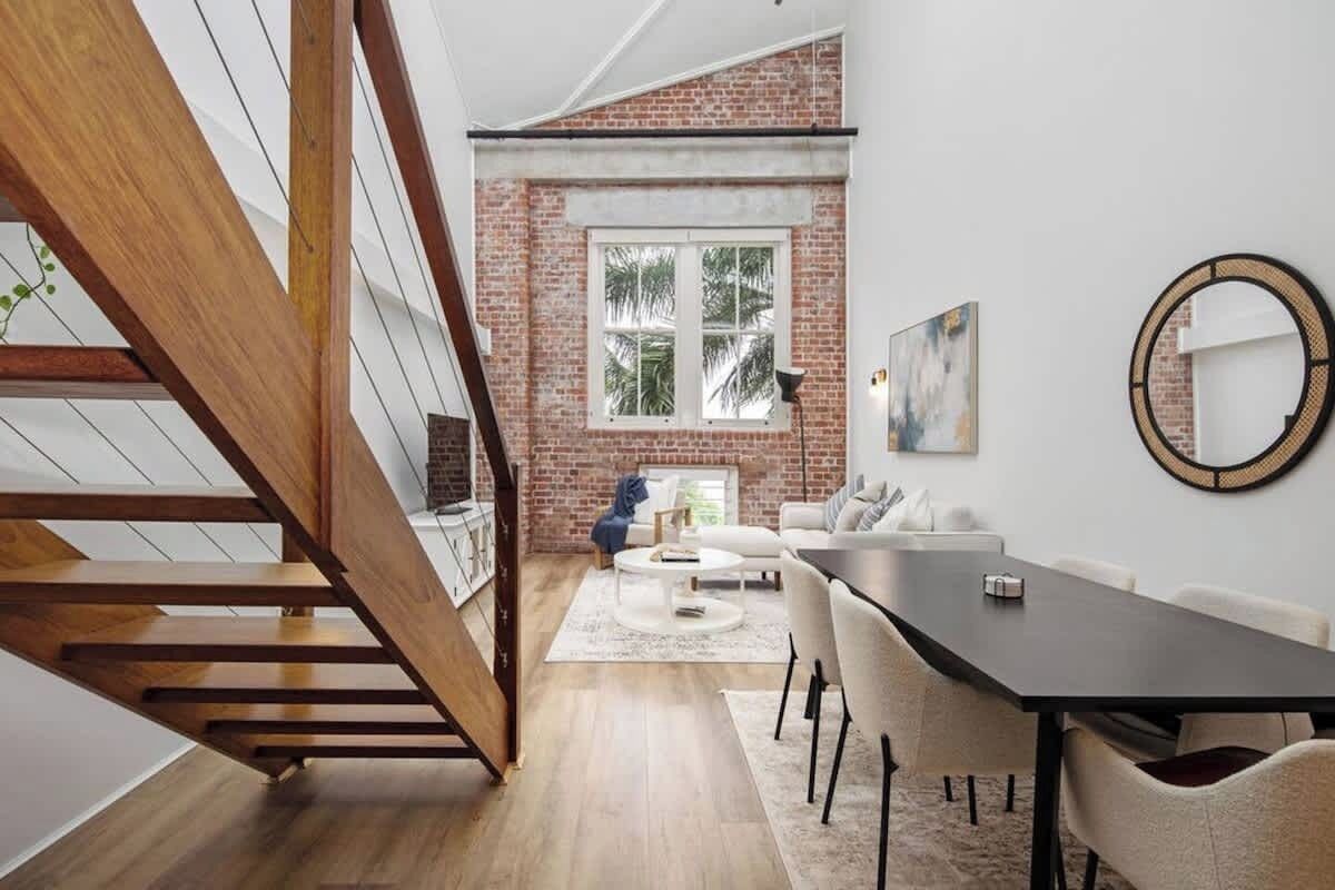 Un interior modern amb una escala, una zona de menjador i una paret de maó.