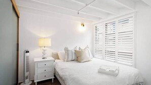 A bedroom with a bed, bedside table, lamp, and a window with blinds. - Woolstore Style! ~ 2bed/2bath/1car ~ Teneriffe (Brisbane)