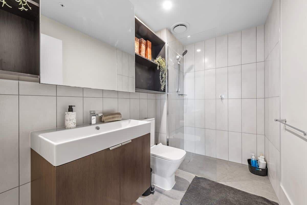 Et moderne badeværelse med en hvid vask, toilet, brusebad og en hylde med toiletartikler.
