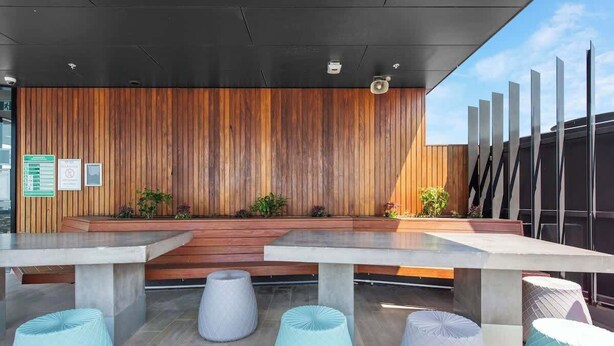 A modern outdoor seating area with wooden panel walls, concrete tables, and light-colored poufs. - Modern Style! 1bed/1bath/balcony/pool ~ CBD (Brisbane)