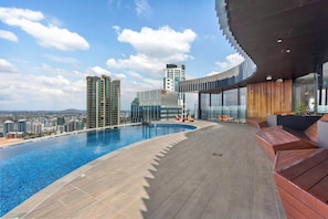 Ein Pool auf dem Dach mit Blick auf die Stadt, moderne Architektur und eine gebogene Glasstruktur.