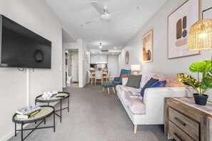 Ein modernes Wohnzimmer mit Flachbildfernseher, Deckenventilator, Sofa, Couchtisch, Essbereich und einer Küche im Hintergrund.