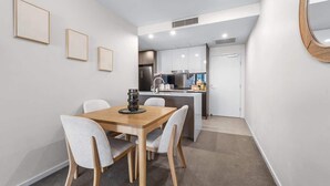 A modern kitchen with white cabinets, a central island, and a dining area with a wooden table and chairs. - Modern Style! 1bed/1bath/balcony/pool ~ CBD (Brisbane)