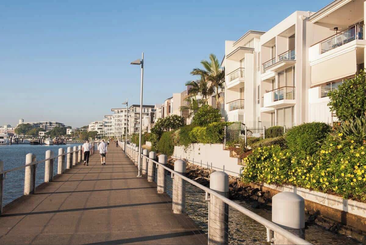 Eine Uferpromenade mit Fußgängerweg, Gebäuden mit Balkonen und blauem Himmel.