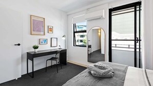 Ein modernes Hotelzimmer mit einem Bett, einem Schreibtisch, einem Stuhl, einer kleinen Pflanze und einem großen Spiegel.