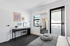 Ein modernes Hotelzimmer mit einem Bett, einem Schreibtisch, einem Stuhl, einer kleinen Pflanze und einem großen Spiegel.