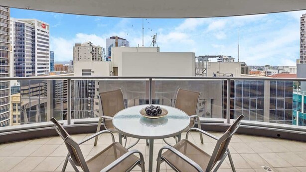 A balcony with a round table and chairs, a bowl of fruit, and a cityscape view. - Inner-city Vibes! 2bed/1bath/1car/balcony~cbd (Brisbane)
