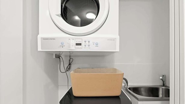 Eine Waschmaschine mit Bedienfeld und einem beige gefärbten Wäschekorb obenauf.