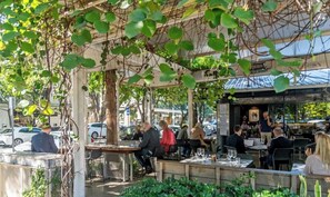An outdoor dining area with tables and chairs, surrounded by greenery and a pergola structure. - Immaculate Top Floor Views! 2bed/2bath/1car/pool (Brisbane)