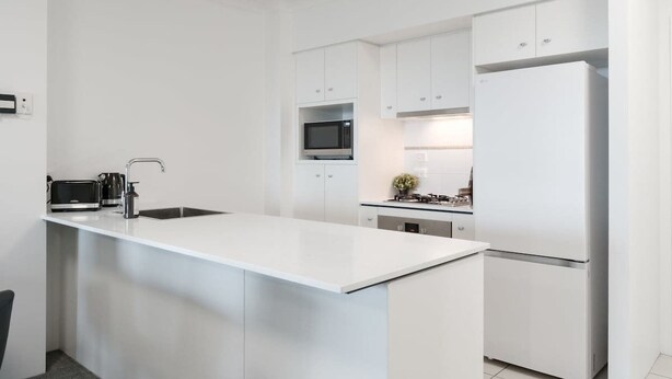 A modern kitchen with white cabinetry, a central island, a microwave, a stove, and a refrigerator. - The Executive! 1bed, 1bath, 1car, Views ~ CBD (Brisbane)