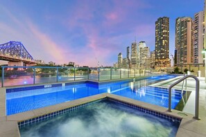 Ein Schwimmbecken mit Stadtansicht und einer Brücke im Hintergrund.