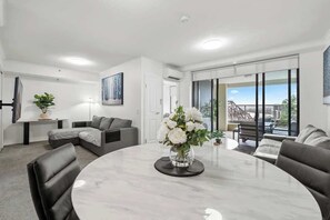 Un salon moderne avec une table ronde en marbre, des canapés gris, une table basse en verre et un vase rempli de fleurs blanches.