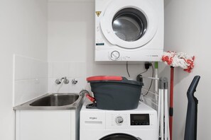 Ein kleiner Waschbereich mit einer Waschmaschine und einem Trockner, einem Spülbecken und einem Wischmopp.