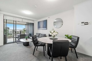 A modern dining area with a round table, black chairs, a vase of flowers, a round mirror, and a city view through large windows. - The Executive! 1bed, 1bath, 1car, Views ~ CBD (Brisbane)