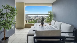 A balcony with a table and sofa, potted plants, and a city view. - The Executive! 1bed, 1bath, 1car, Views ~ CBD (Brisbane)