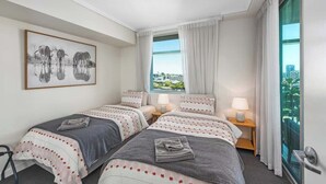 Une chambre d’hôtel avec deux lits, une vue sur la ville, un tableau encadré au mur et une fenêtre avec des rideaux.
