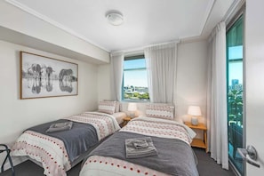 Ein Hotelzimmer mit zwei Betten, Blick auf die Stadt, einem gerahmten Bild an der Wand und einem Fenster mit Vorhängen.