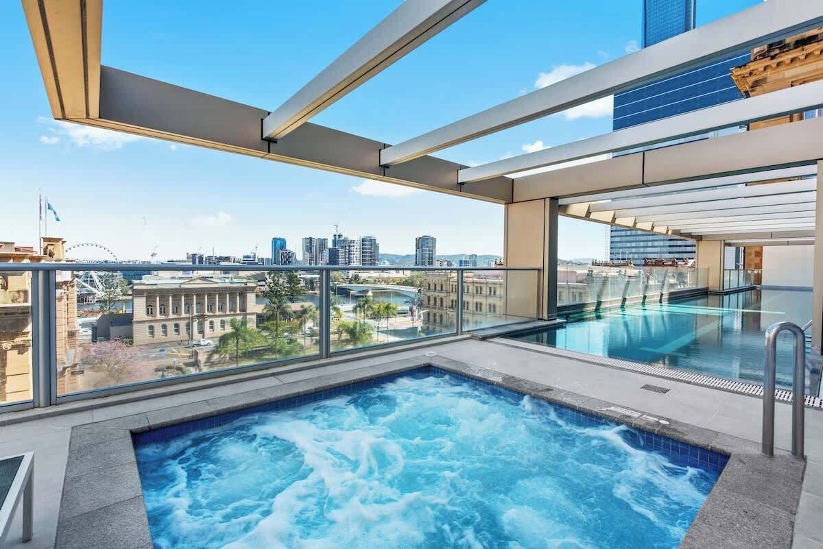 Una piscina en la azotea con vista a la ciudad, barandilla de cristal y diseño arquitectónico moderno.