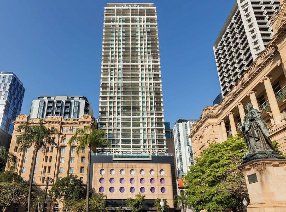 A tall hotel with a modern glass facade, surrounded by historic buildings and a statue.
