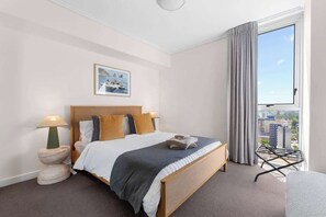 A hotel room with a bed, a side table with a lamp, a window with curtains, and a city view. - City Escape! 2bed-2bath-1car-pool-views - CBD (Brisbane)