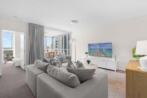 Ein modernes Wohnzimmer mit einem grauen Sofa, einem Essbereich mit Stühlen, einem großen Gemälde und Blick durch eine Glastür.