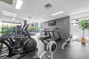 Ein Fitnessstudio mit Trainingsgeräten, großen Fenstern und einem Flachbildfernseher.