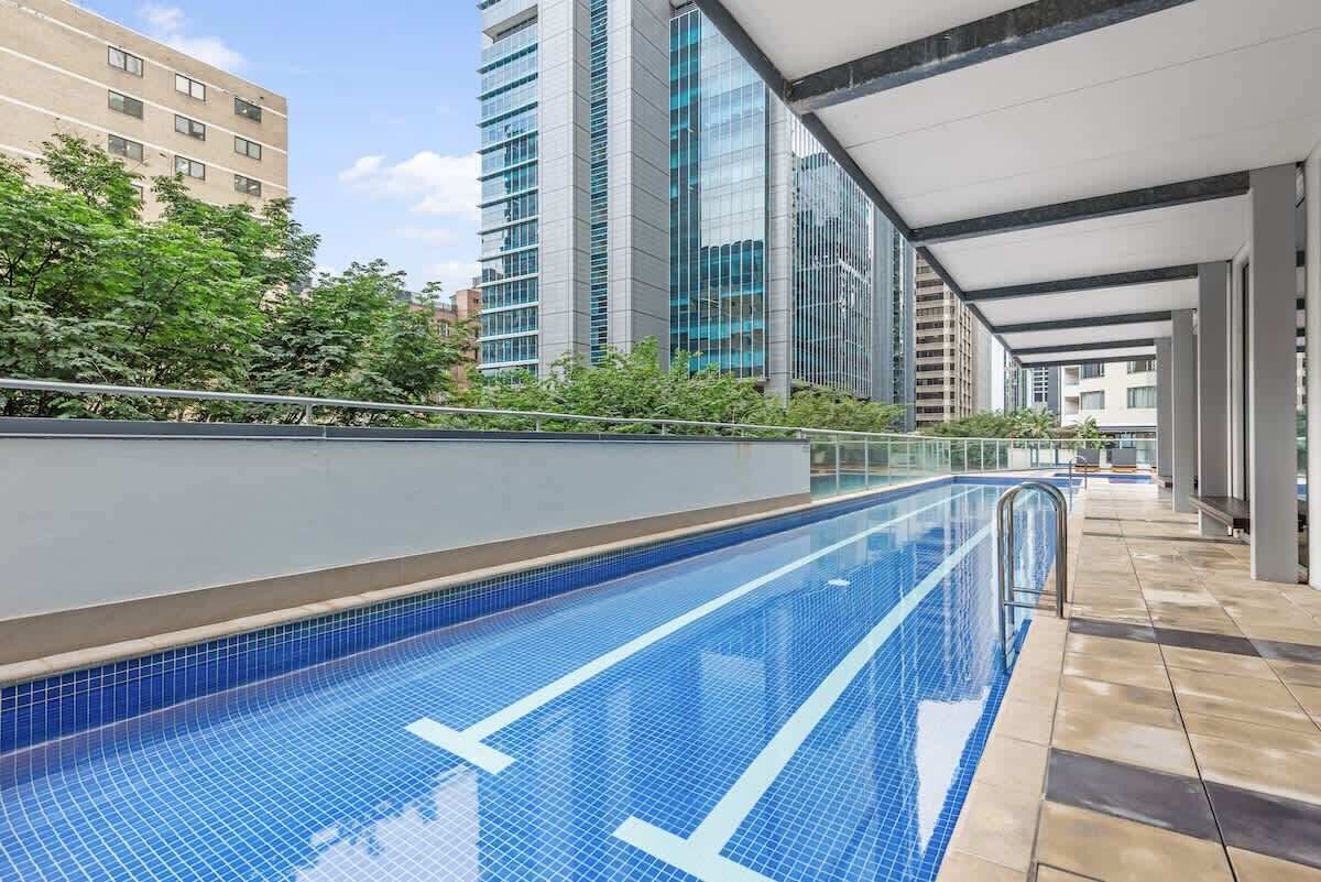 A swimming pool with a tiled floor, surrounded by a covered walkway and modern buildings.
