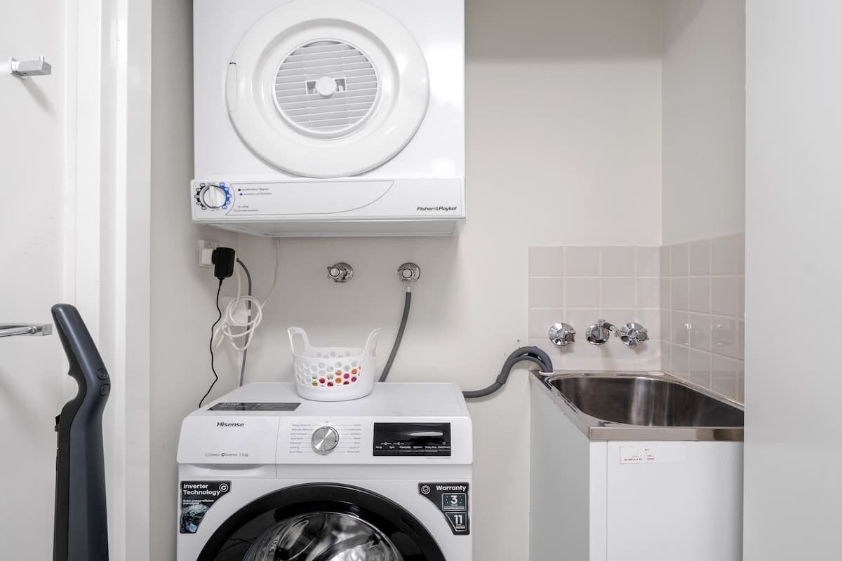 A compact laundry area with a front-loading washer, a stacked dryer, and a stainless steel sink.