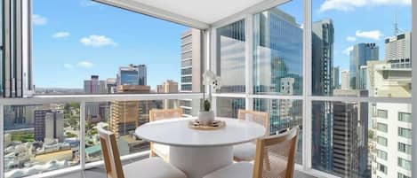 A modern room with a round table and chairs, large windows with a city view, and a ceiling light.