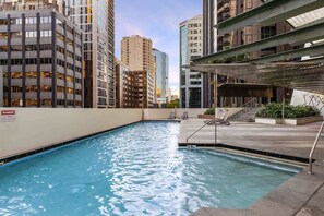 Une piscine sur le toit, agrémentée d’un panneau indiquant « Il est interdit de sauter », et entourée d’immeubles de grande hauteur.