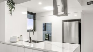 A modern kitchen with white cabinetry, stainless steel appliances, and a large island. - Amazing! 2bed/2bath/1car/balcony/views ~ CBD (Brisbane)