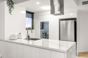 A modern kitchen with white cabinetry, stainless steel appliances, and a large island. - Amazing! 2bed/2bath/1car/balcony/views ~ CBD (Brisbane)