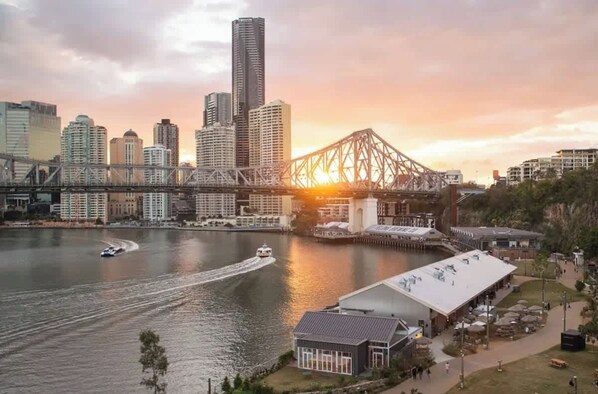 A waterfront cityscape with a prominent bridge, high-rise buildings, and a boat on the water. - Amazing! 2bed/2bath/1car/balcony/views ~ CBD (Brisbane)