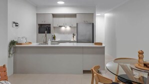 A modern kitchen with white cabinetry, a stainless steel refrigerator, and a glass dining table. - Skyline Stunner! 3bed/2bath/1car/views ~ CBD (Brisbane)