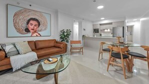 A modern living room with a glass coffee table, a brown leather sofa, and a dining area with wooden chairs. - Skyline Stunner! 3bed/2bath/1car/views ~ CBD (Brisbane)