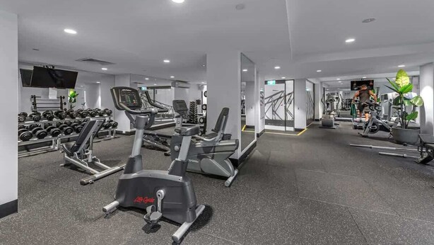 A modern gym with cardio machines, free weights, and a TV screen. - Skyline Stunner! 3bed/2bath/1car/views ~ CBD (Brisbane)